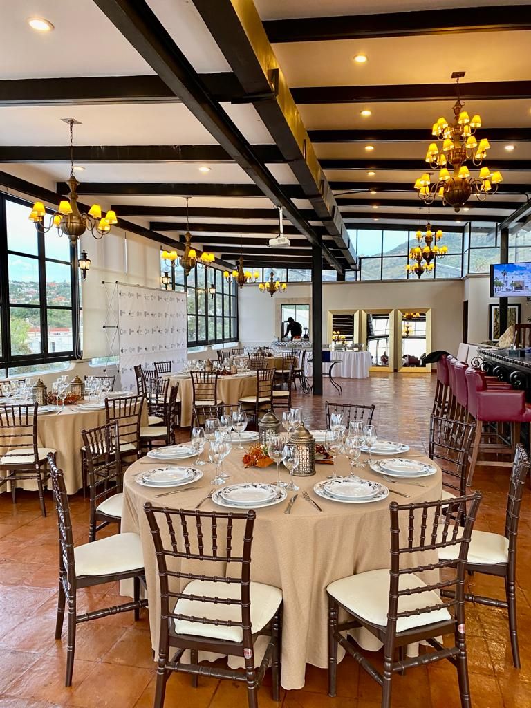 A spacious dining area with round tables set for a meal, large windows, and a high ceiling with exposed beams.