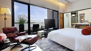 A modern hotel room with a large bed, a TV, a desk, and a seating area with chairs.