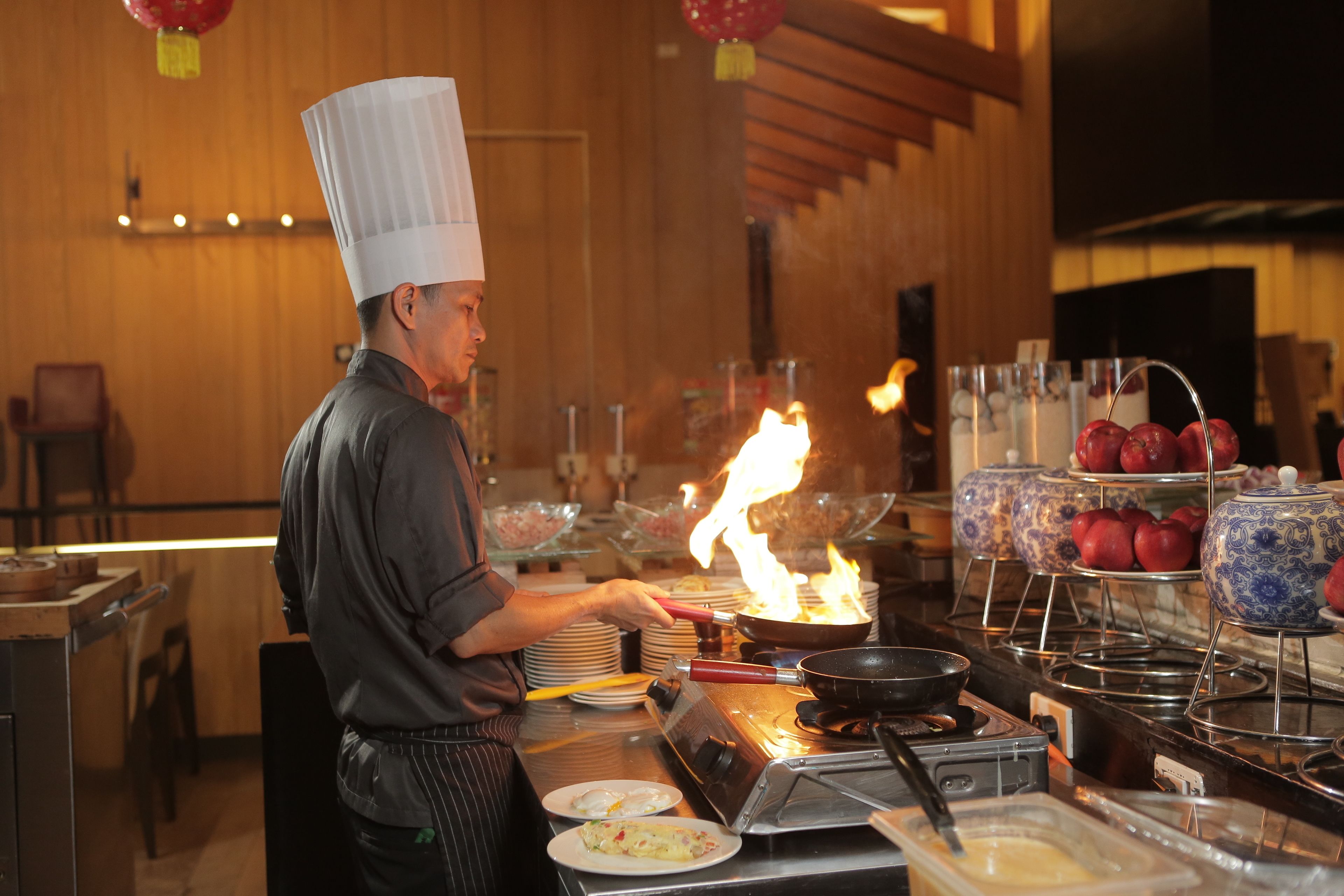 A chef cooking with a flame, surrounded by kitchen equipment and food items.