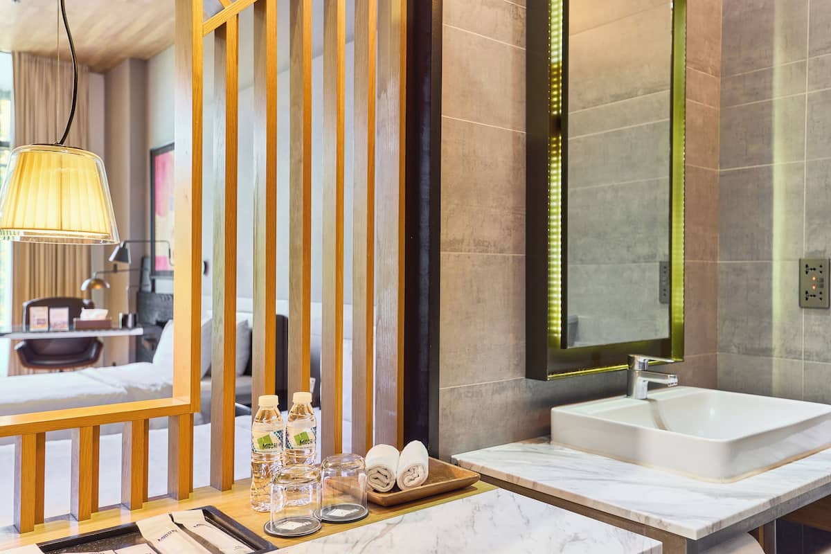A modern hotel bathroom with a large mirror, a sink, and a vanity. There are toiletries on the counter, including bottles and towels.