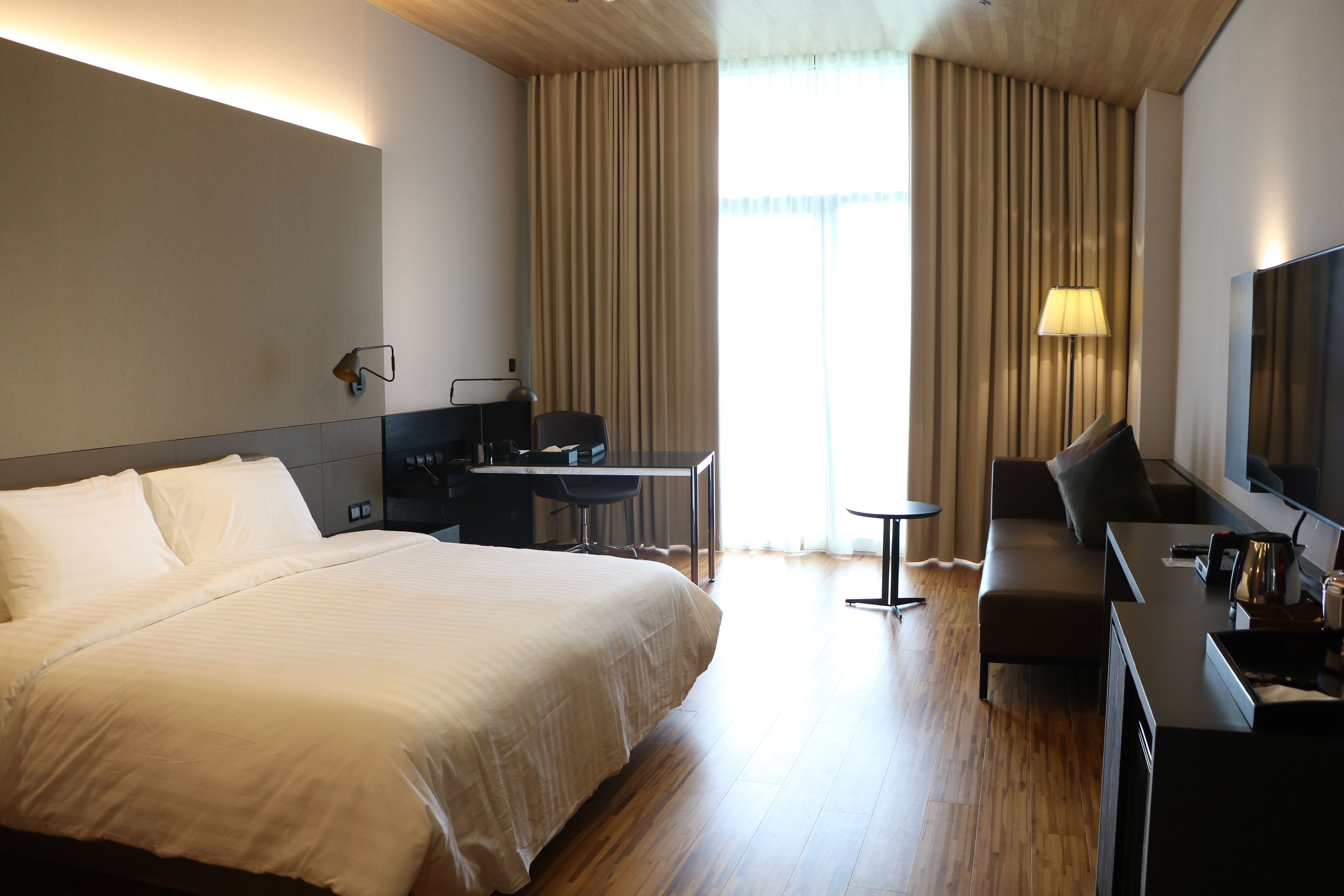 Camera d'albergo con un letto grande, una scrivania, un divano, una TV e una finestra con tende.