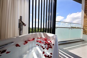 Un baño con una bañera llena de pétalos de rosa, ducha y balcón con barandilla de cristal.