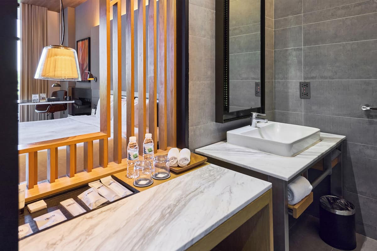 A modern bathroom with a marble countertop, a white sink, and a wooden vanity. There are bottles of water and towels on the counter.