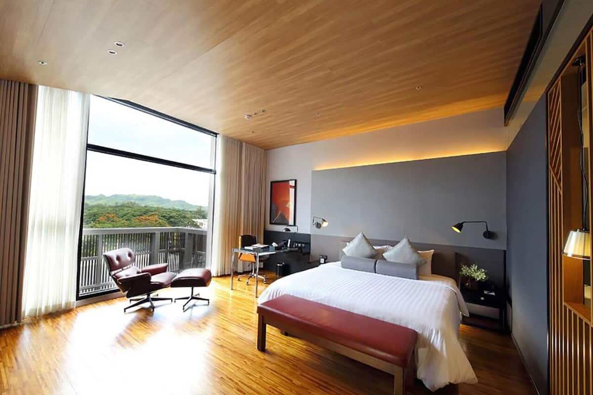 A modern hotel room with a large bed, a desk, and a view of the outdoors.
