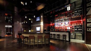 A modern bar area with a bar counter, multiple stools, and a well-stocked shelf of bottles.