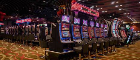 Una hilera de máquinas tragamonedas en un casino, con alfombra estampada y diseño de techo moderno.