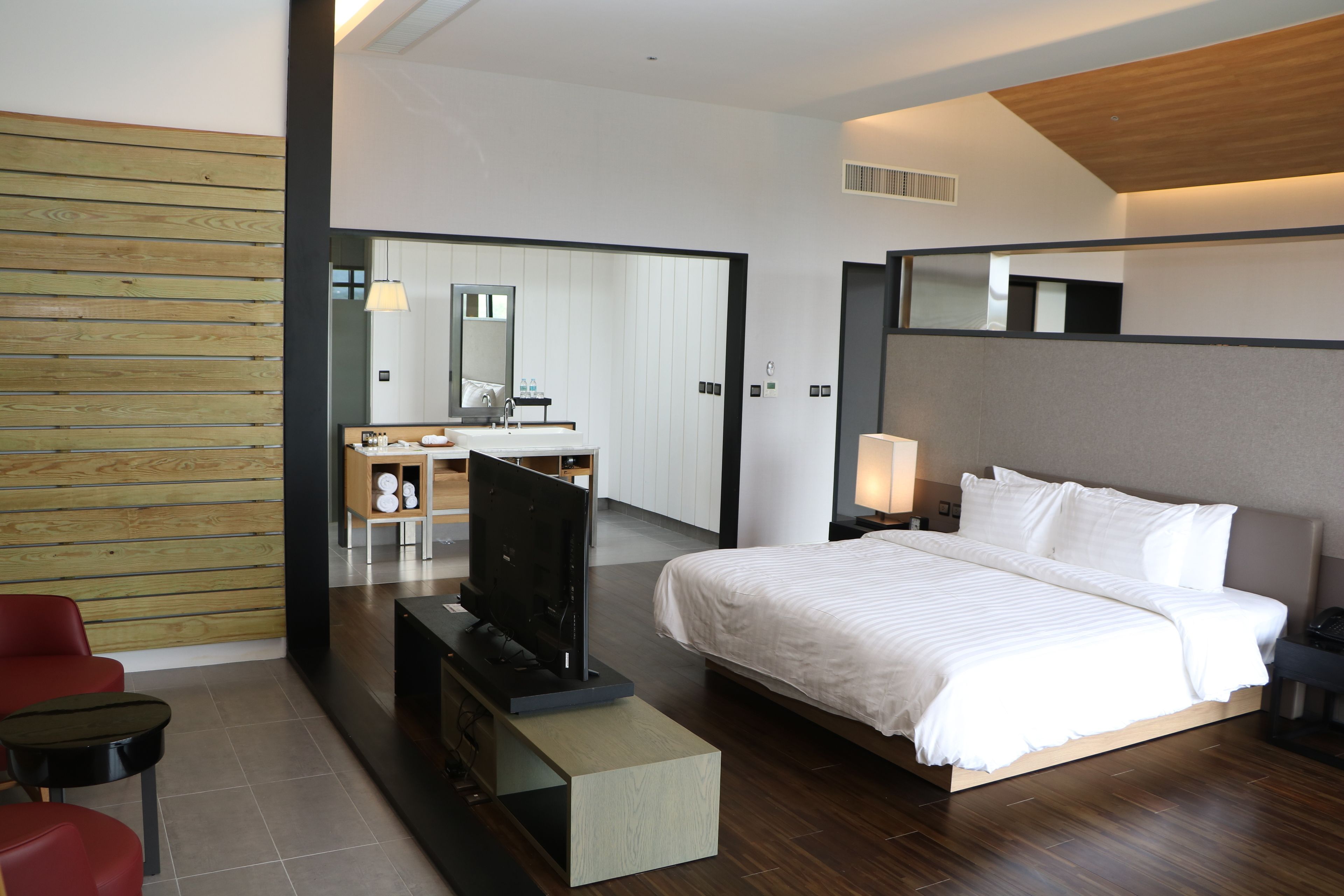 A modern hotel room with a large bed, a TV on a stand, a desk with a chair, and a wooden panel wall.