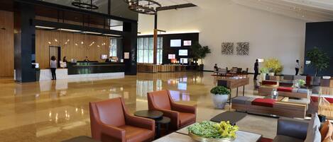 A spacious lobby with a reception desk, seating areas, and a modern chandelier.