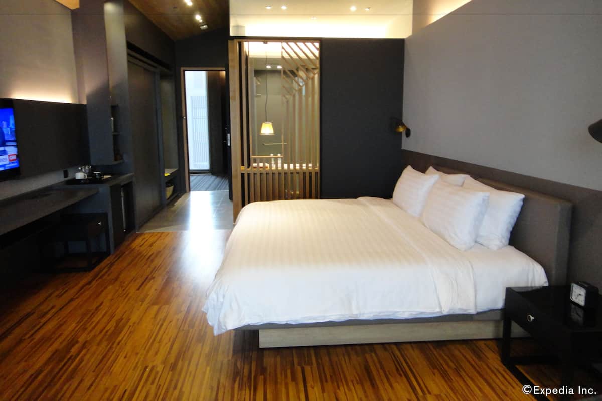 A modern hotel room with a large bed, a TV, and a wooden floor.