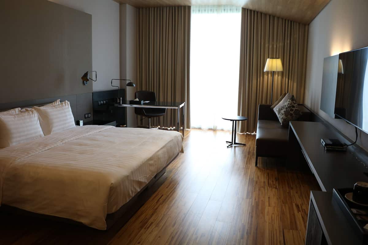 A hotel room with a large bed, a desk with a chair, a sofa, a TV, and a window with curtains.