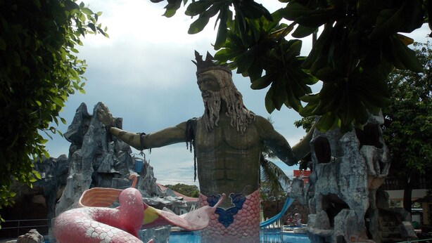 Una grande statua raffigura una figura con le braccia tese e una coda da sirena, circondata da rocce e una vasca.