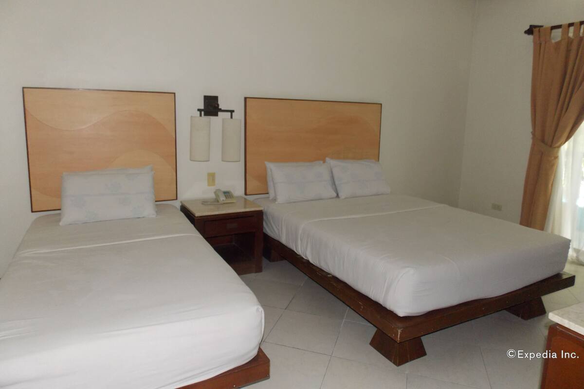 A hotel room with two single beds, a nightstand with a phone, and a wall-mounted light fixture.
