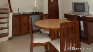 Un'area pranzo con tavolo e sedie in legno, una cucina con frigorifero e un televisore su un mobiletto in legno.
