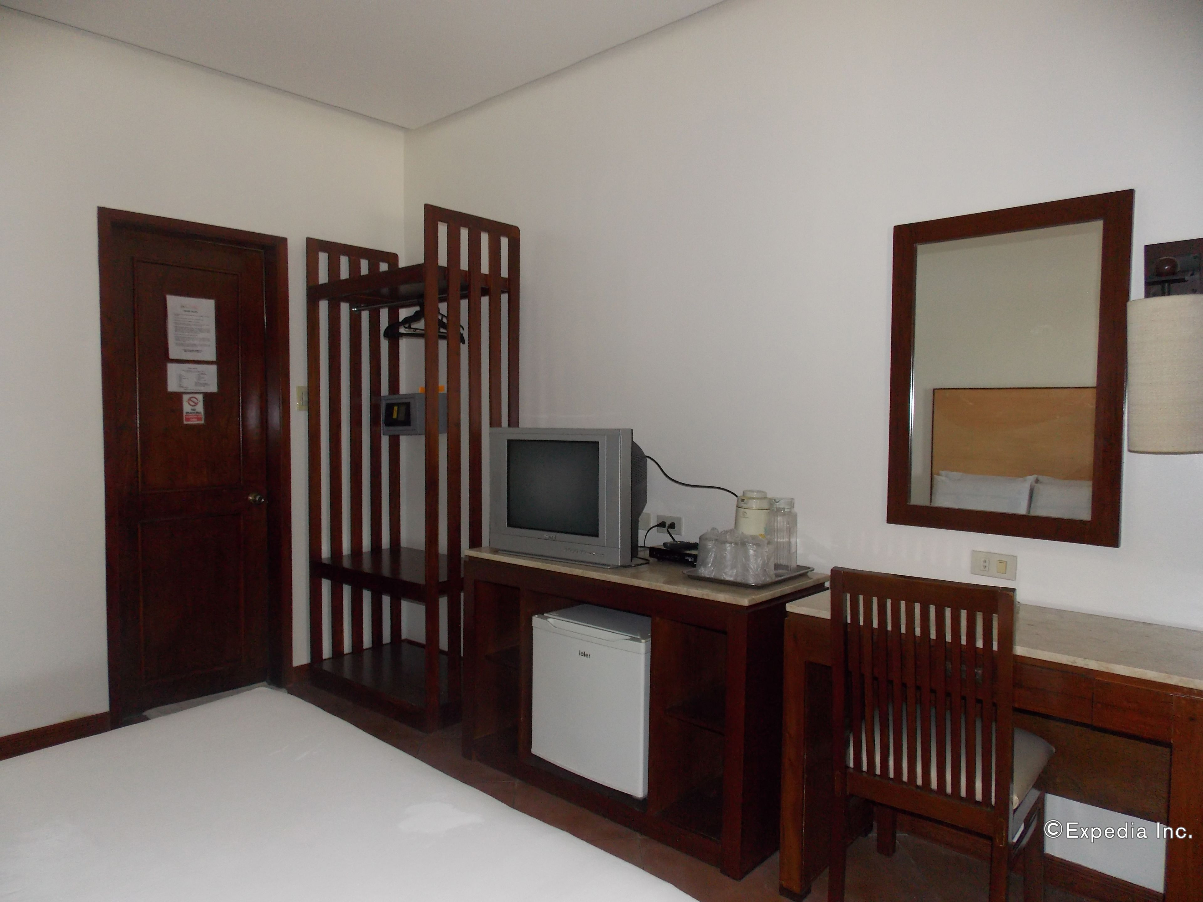 Habitación de hotel con escritorio de madera, televisor, refrigerador pequeño, silla y espejo en la pared.
