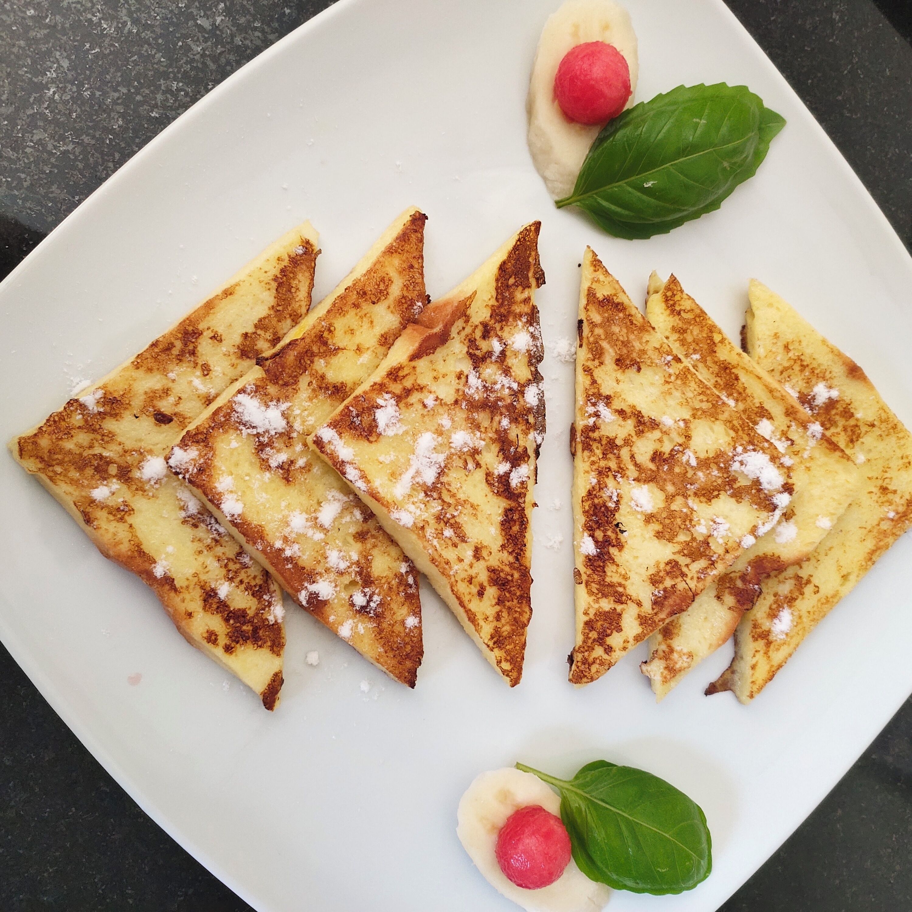 A plate of triangular-shaped pancakes with powdered sugar and a red fruit garnish.