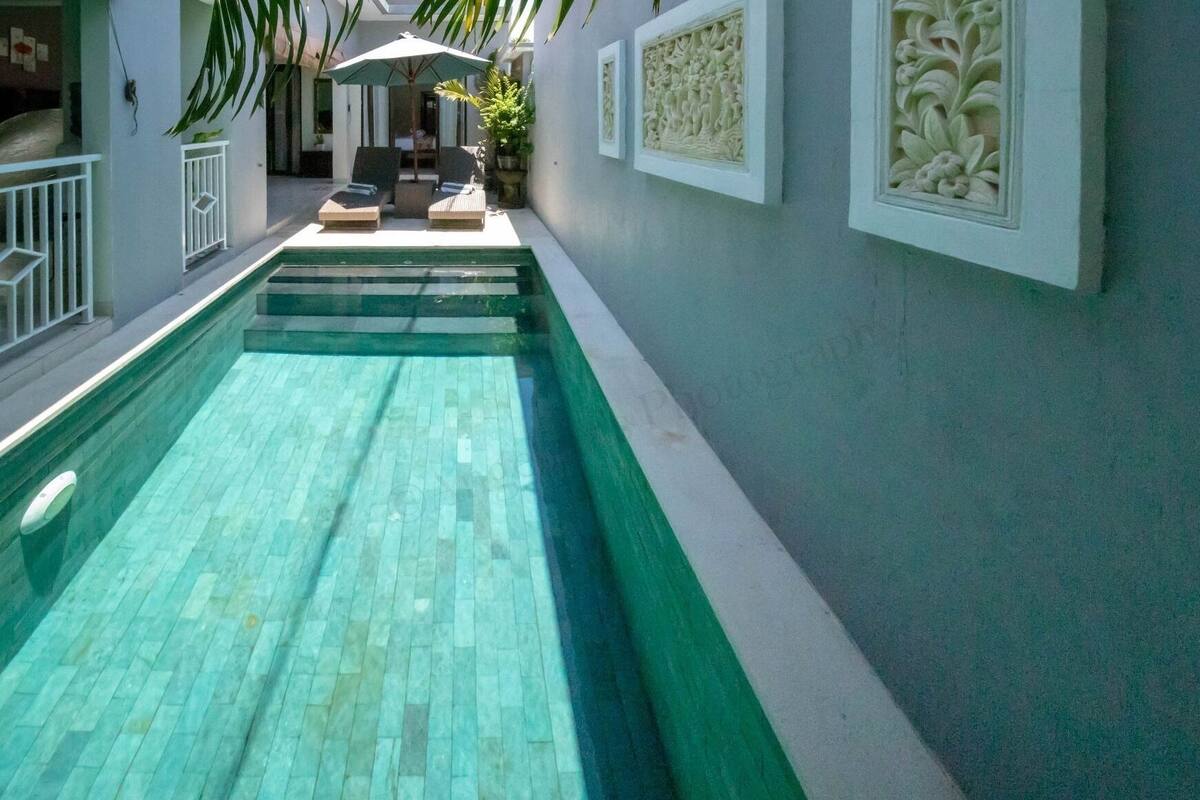 A swimming pool with a tiled deck, a lounge area with chairs and an umbrella, and decorative wall carvings.