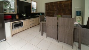 A modern kitchen with a stainless steel refrigerator, a built-in oven, and a black countertop. There is a wicker partition and a water dispenser on the wall. - Bahagia Villas (Denpasar)