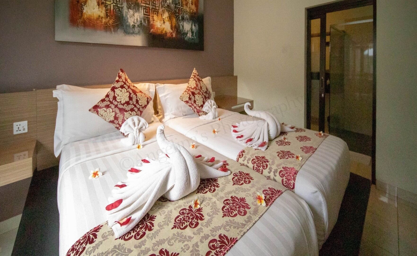 A hotel room with two beds, each with floral-patterned bedding and towels arranged in a swan shape.