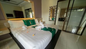 A hotel room with a large bed, a mirror, a television, and a sliding door to the bathroom. - Bahagia Villas (Denpasar)