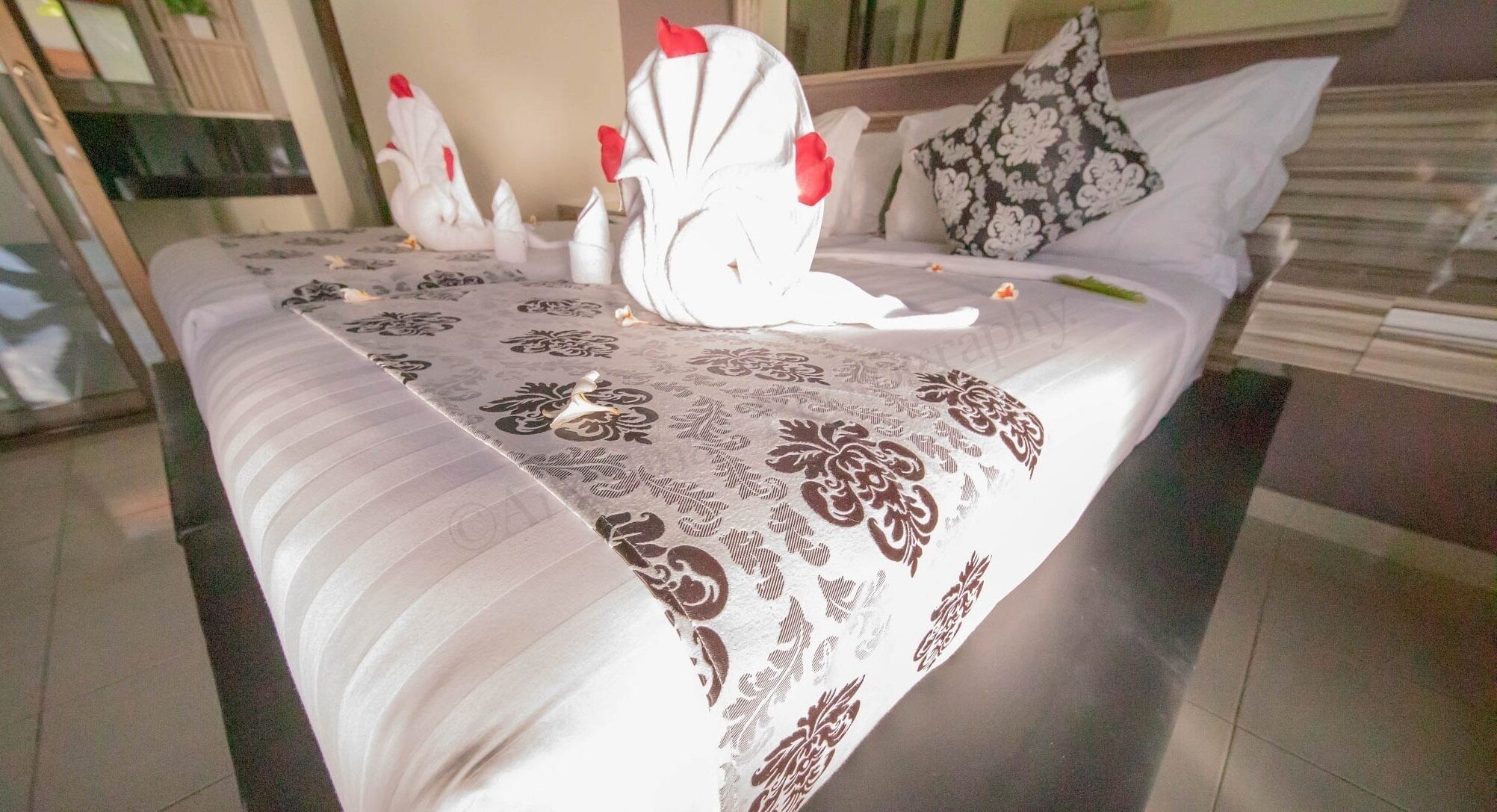 A neatly made bed with a floral-patterned bedspread, two white swan-shaped pillows, and a black and white patterned pillow.