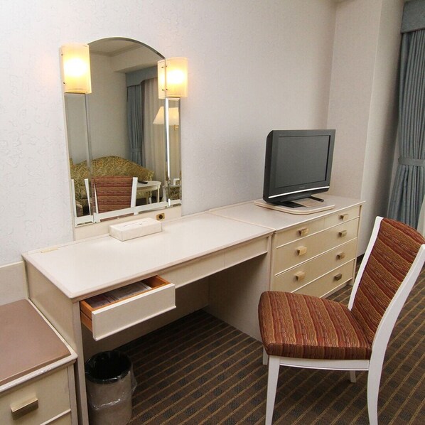 Habitación de hotel con un escritorio blanco, televisor, espejo, silla y cubo de basura.