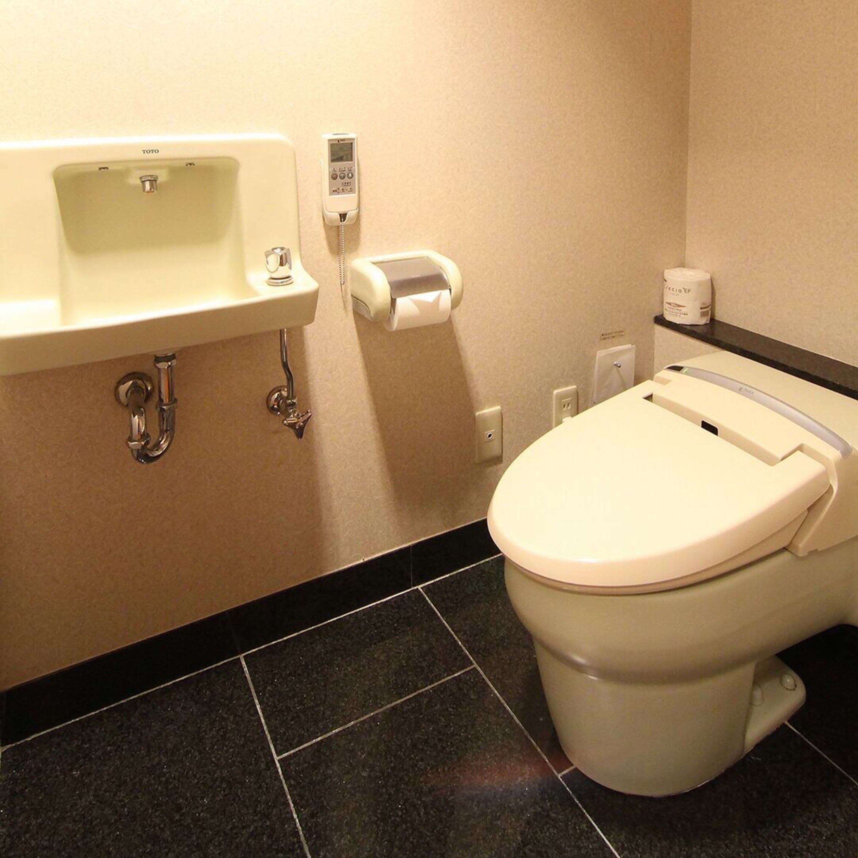 A bathroom with a toilet, sink, and paper towel dispenser.