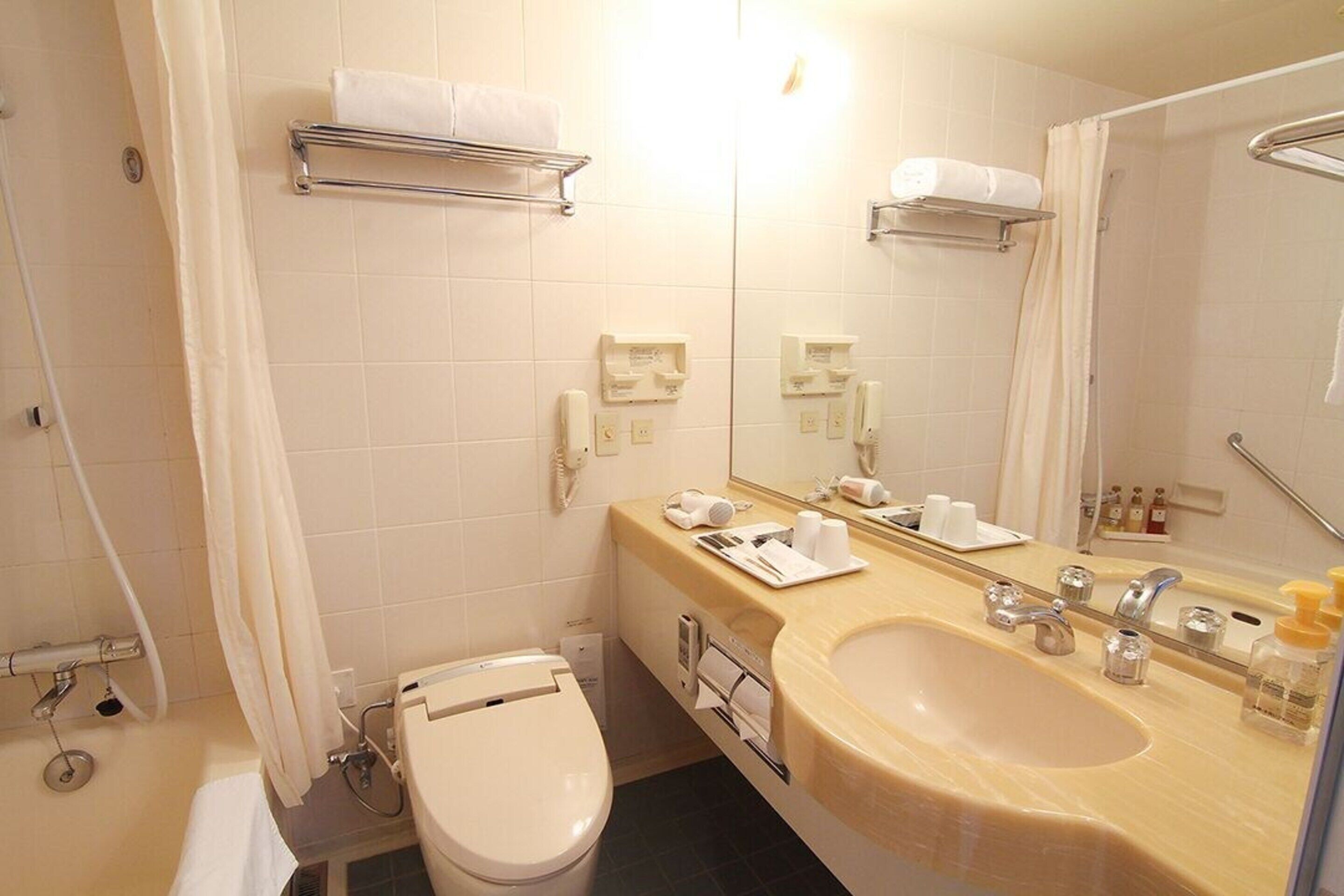 A bathroom with a toilet, sink, and mirror. There are towel racks and a shower curtain.