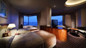 Habitación de hotel con dos camas, un escritorio, televisión y vistas a la ciudad.