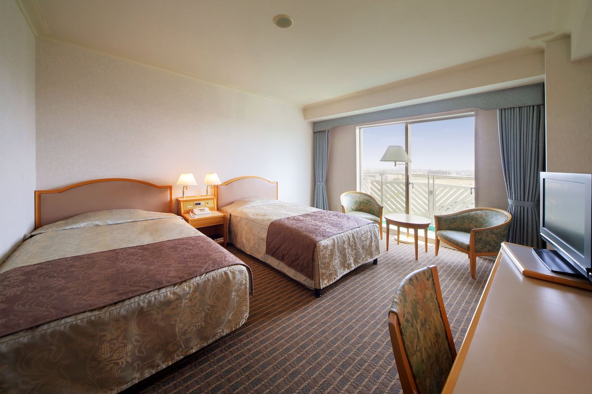 A hotel room with two beds, a desk, a chair, a television, and a window with curtains.