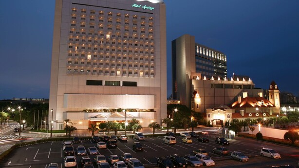 Un hotel de diseño moderno, con un amplio estacionamiento y varios edificios al fondo.