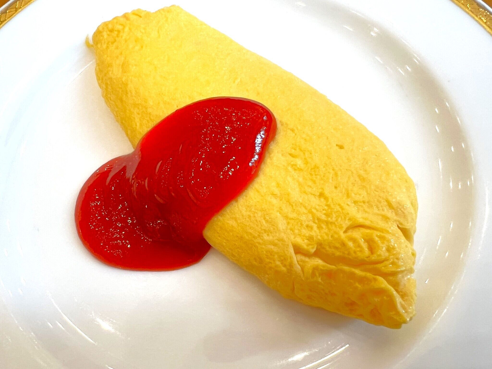 A plate with a rolled omelette and a dollop of red sauce.
