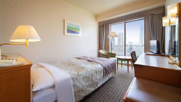 Una habitación de hotel con cama, escritorio, silla, lámpara de escritorio, teléfono y ventana con vista a un edificio.