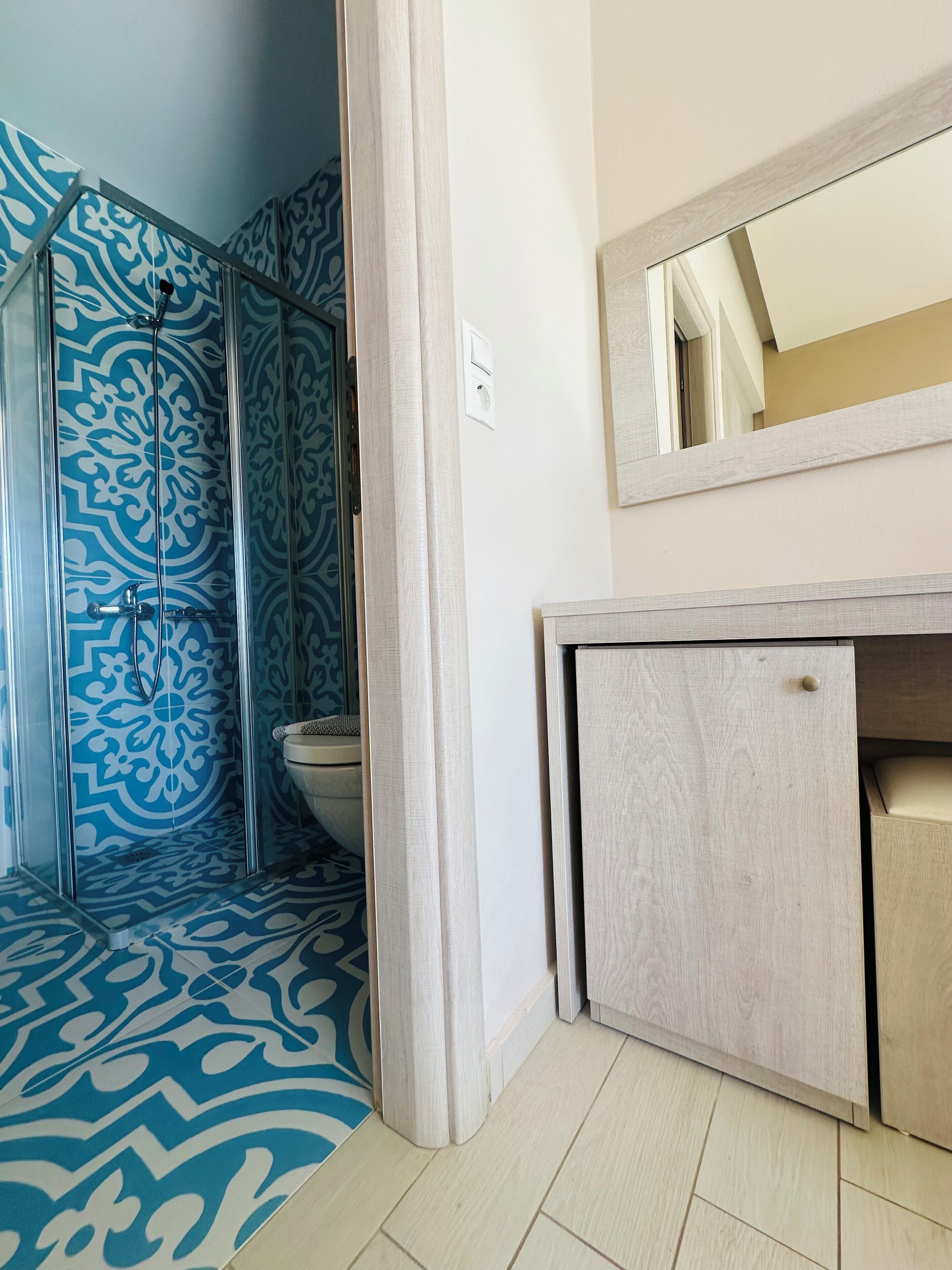 A bathroom with a patterned shower wall, a toilet, and a mirror above a wooden vanity.