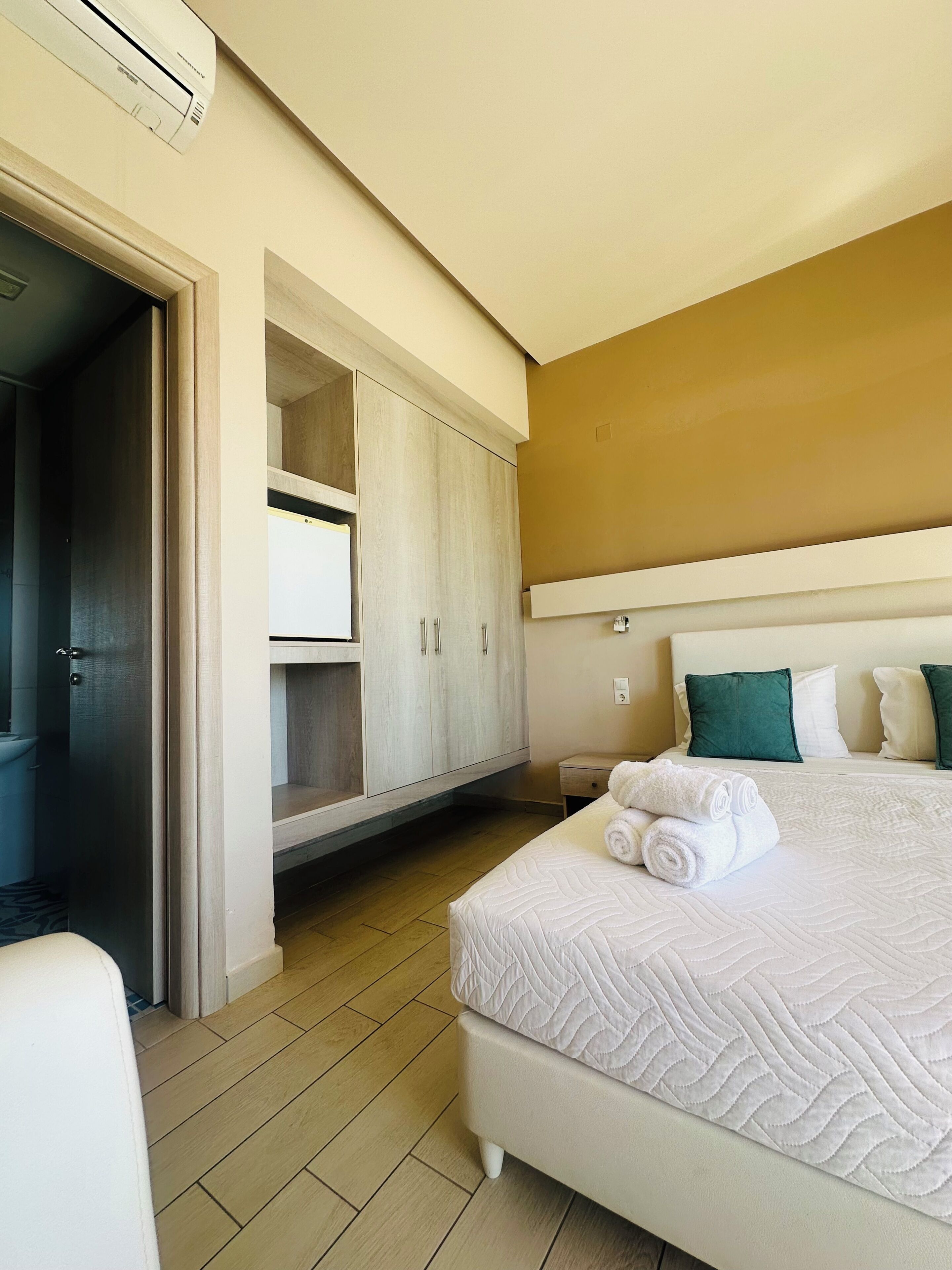 A hotel room with a bed, a wardrobe, a small table, and a wall-mounted air conditioner.