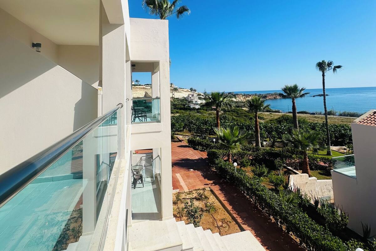 A modern hotel with a glass staircase, a pool, and a view of the sea.