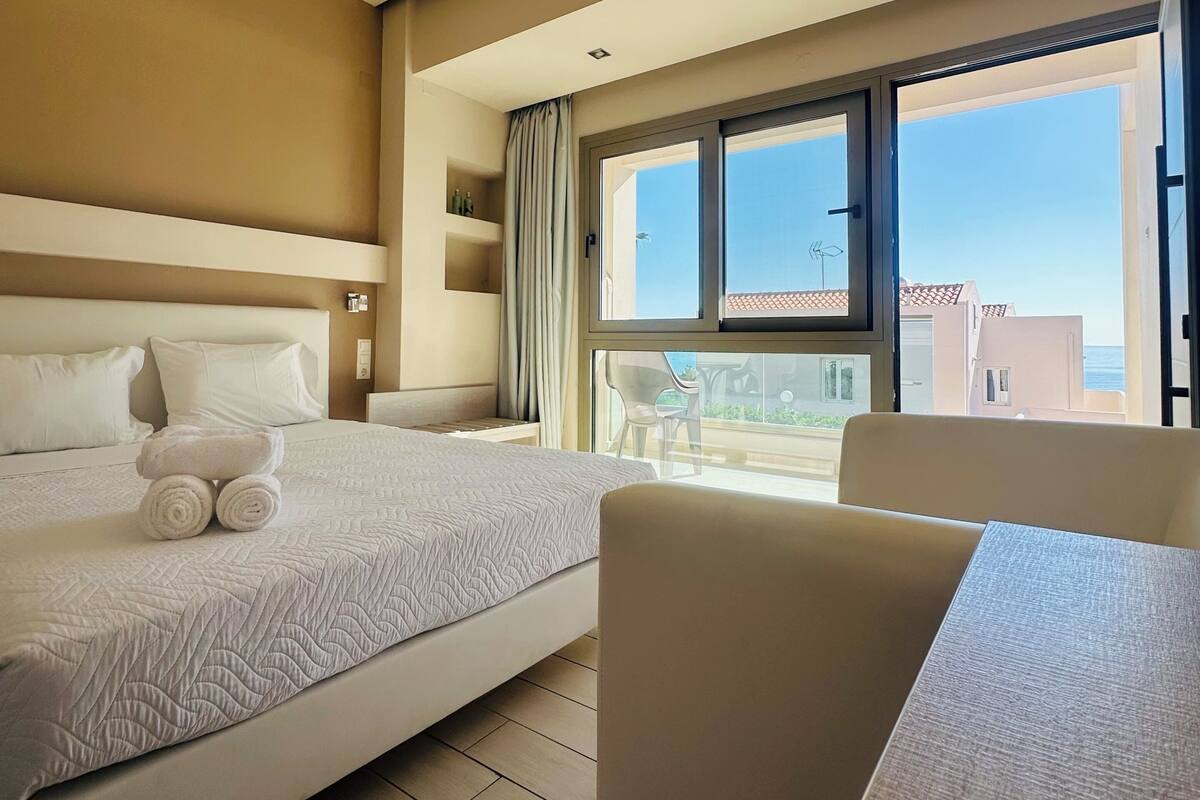 A hotel room with a large bed, a balcony with a table and chairs, and a view of the outside.