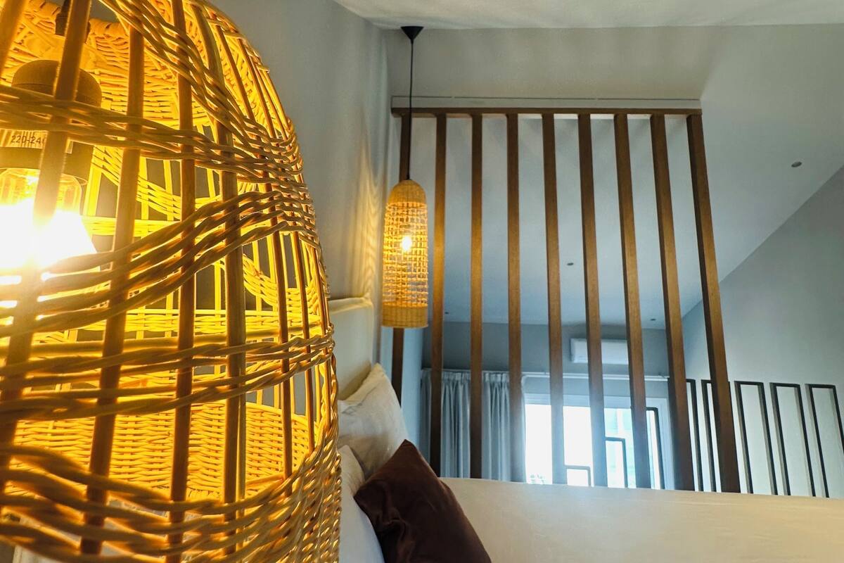 A room with a bed, a hanging wicker lamp, and a ceiling light.