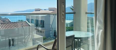 A balcony with a glass door, a table with chairs, and a view of the sea and buildings.