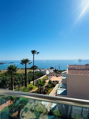 Ein Balkon mit freiem Blick auf das Meer, Palmen und ein Gebäude mit Ziegeldach.