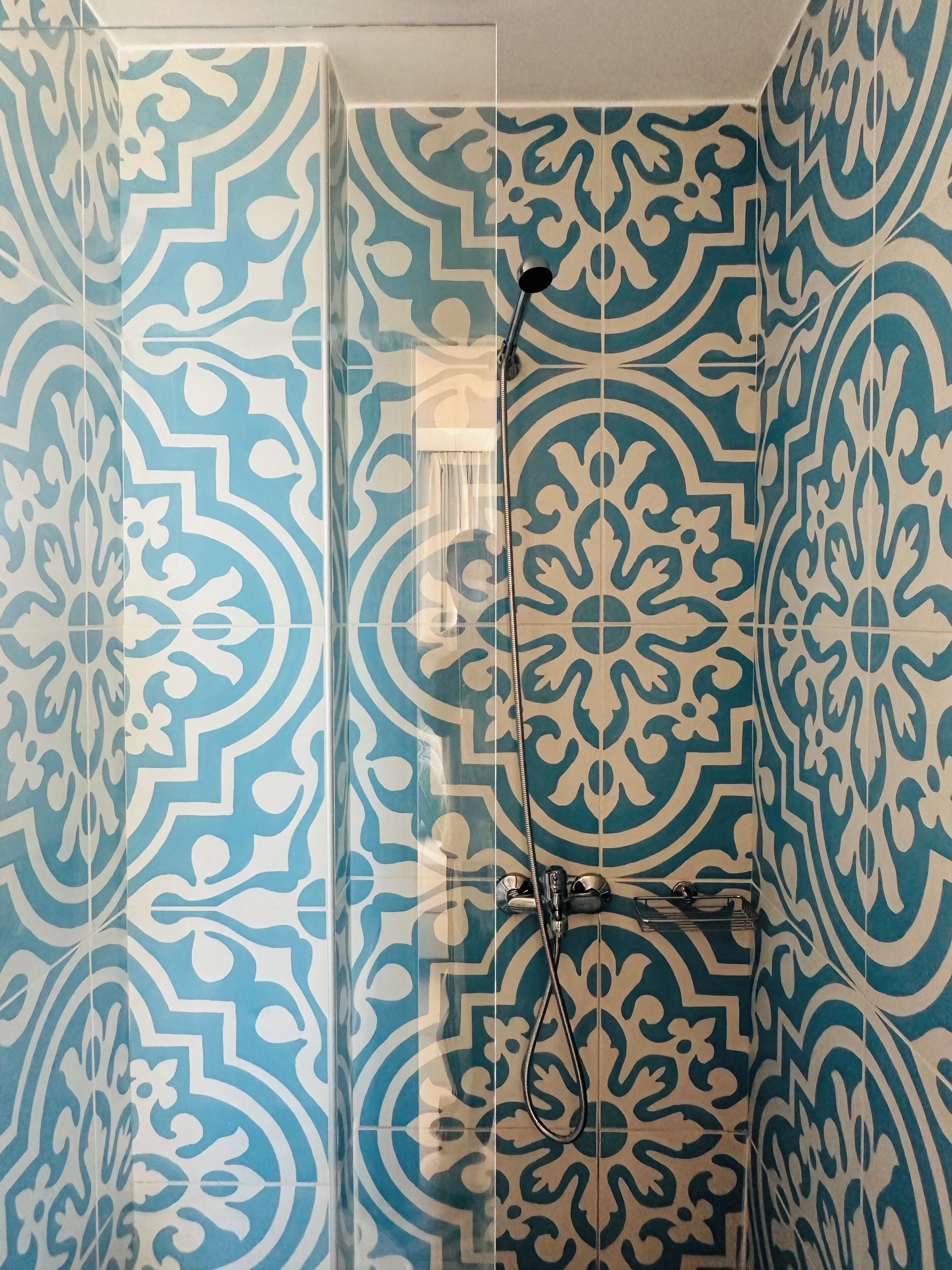 A shower with a patterned tile wall, a handheld showerhead, and a glass door.