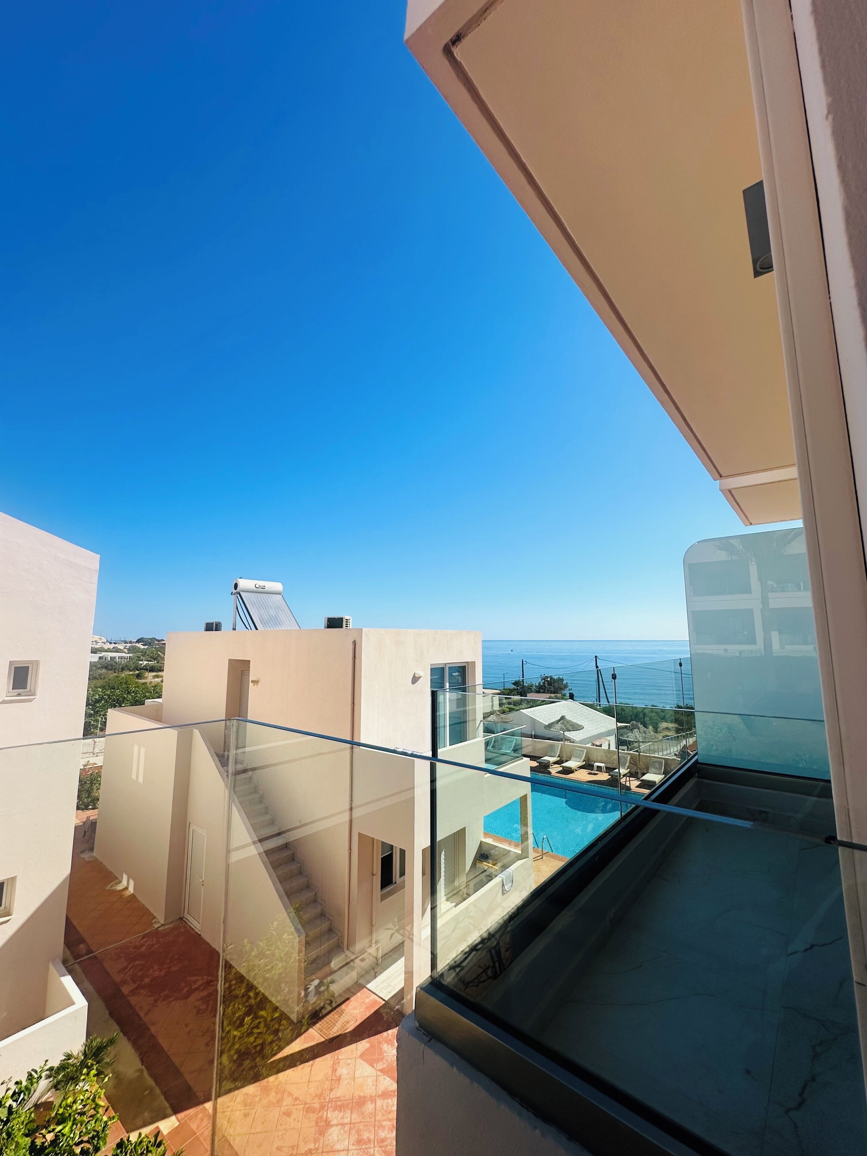 Un balcon doté d’une balustrade en verre, donnant sur une piscine et un ciel d’un bleu limpide.