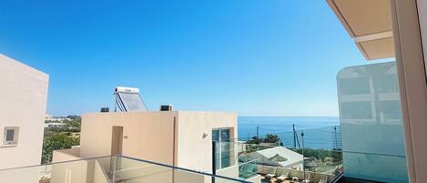 Un balcon doté d’une balustrade en verre, donnant sur une piscine et un ciel d’un bleu limpide.