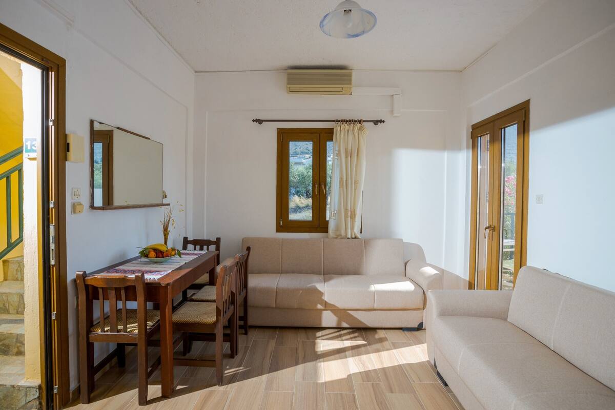A room with a sofa, dining table, chairs, and a window with curtains.