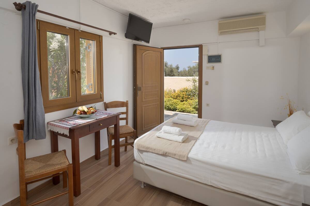 A bedroom with a bed, a desk with a chair, a window with curtains, and a television mounted on the wall.