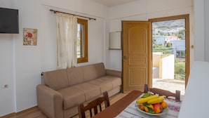 A room with a sofa, a dining table with fruit, a TV, and a door leading to an outdoor area. - Bellino Apartments - Adults Only (Hersonissos)