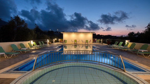 A swimming pool with a tiled deck, surrounded by green lounge chairs and a covered seating area with tables and chairs. - Bellino Apartments - Adults Only (Hersonissos)
