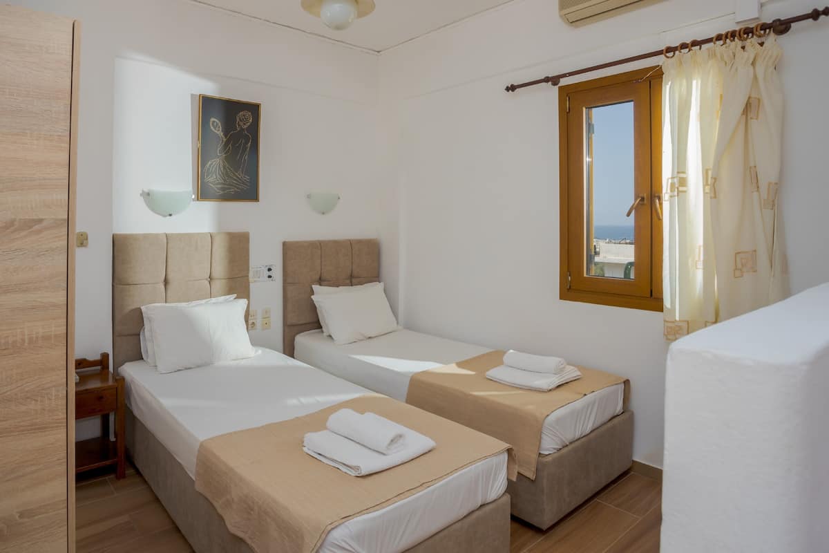 A hotel room with two single beds, a wooden headboard, a small desk, and a window with curtains.