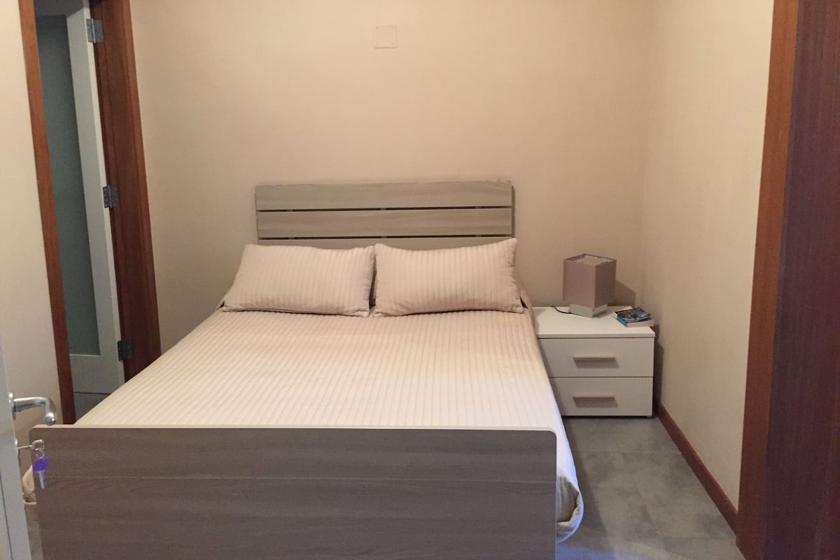 A small, neatly arranged bedroom with a bed, bedside tables, and a nightstand.
