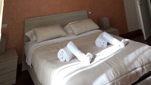 A neatly made bed with white linens and two rolled towels, a bedside table with a lamp, and a wooden headboard. - B&B Chez Moi (Naples)