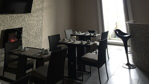 A dining area with a fireplace, a TV mounted on the wall, and a bar stool. - B&B Chez Moi (Naples)